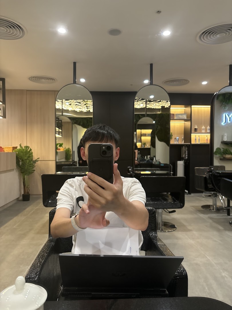 A person takes a selfie inside a modern, well-lit hair salon with stylish mirrors and seating.
