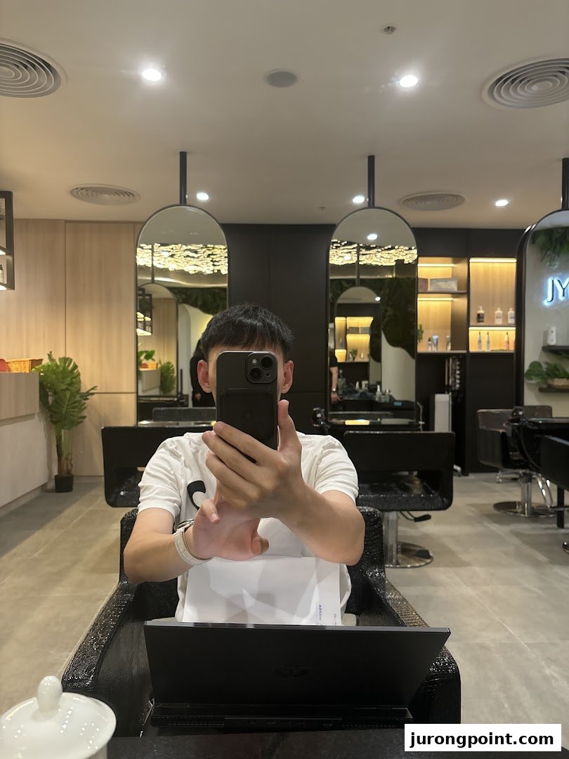 A person takes a selfie inside a modern, well-lit hair salon with stylish mirrors and seating.