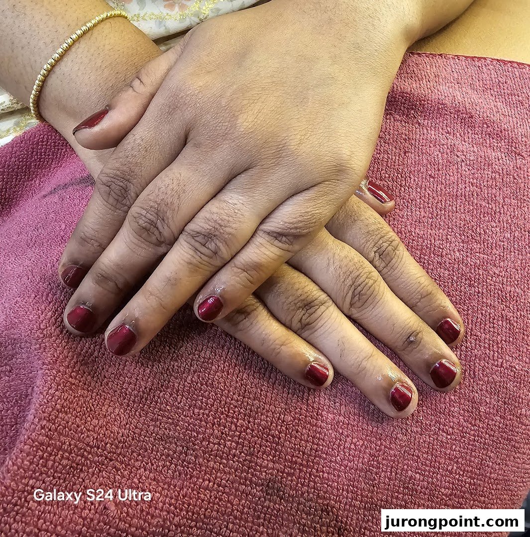 Close-up of hands with freshly painted red nails resting on a pink towel.