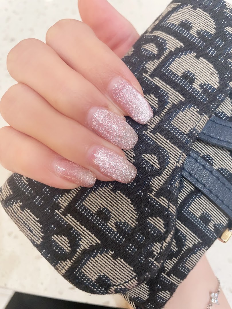 A hand showcasing elegant glitter nail polish, held against a patterned accessory.