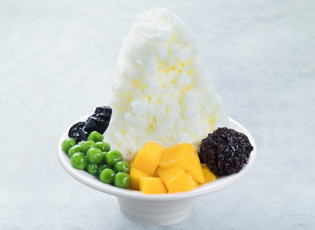 A vibrant shaved ice dessert with mango, green pearls, grass jelly, and black glutinous rice.