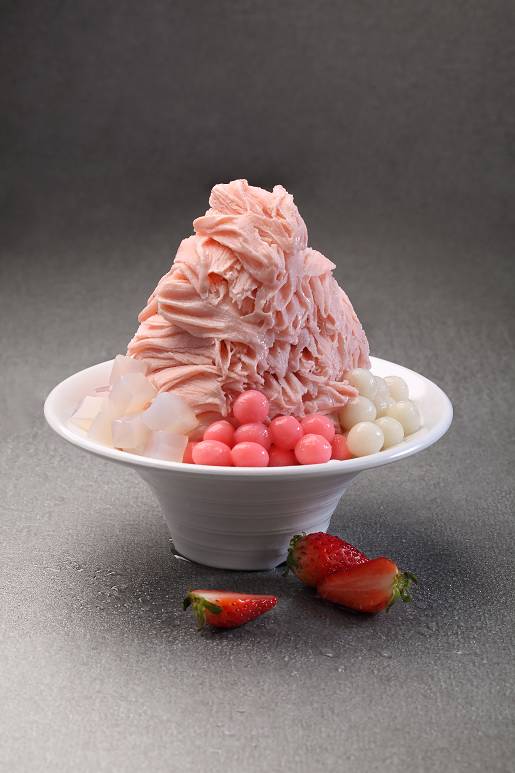 A vibrant bowl of pink shaved ice dessert with various toppings and fresh strawberries.