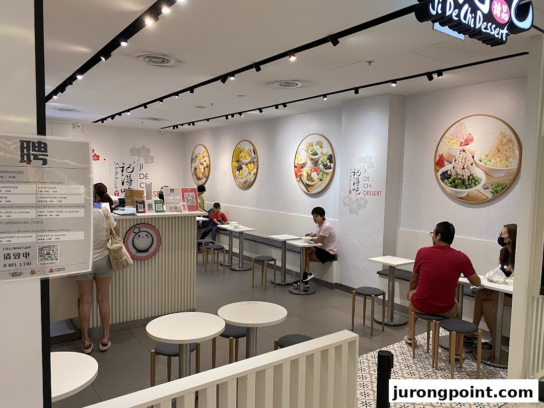 Interior view of Ji De Chi Dessert, featuring customers, seating, and vibrant dessert wall art.