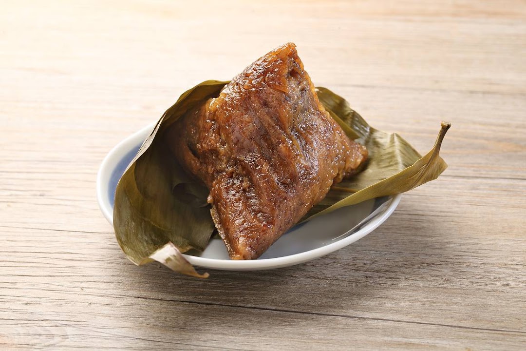 A traditional sticky rice dumpling (zongzi) wrapped in bamboo leaves, served on a white plate.