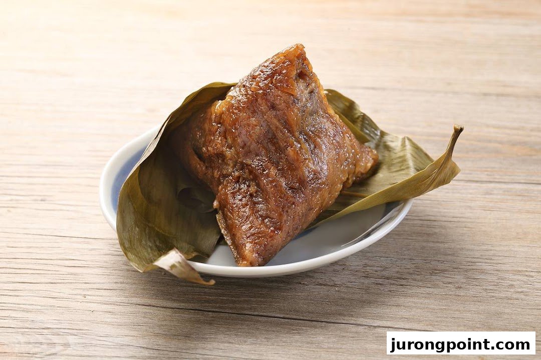 A traditional sticky rice dumpling (zongzi) wrapped in bamboo leaves, served on a white plate.