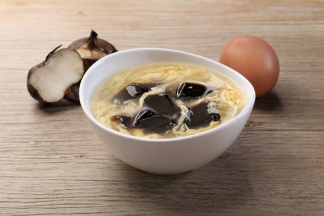 A bowl of traditional Chinese dessert soup with egg and herbal jelly, alongside fresh ingredients.