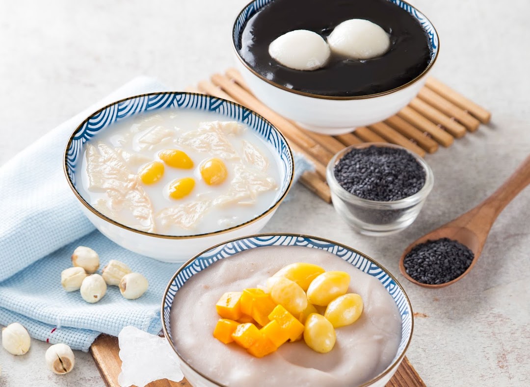 Three bowls of traditional Asian desserts, including black sesame soup, ginkgo nut, and taro/yam puddings.