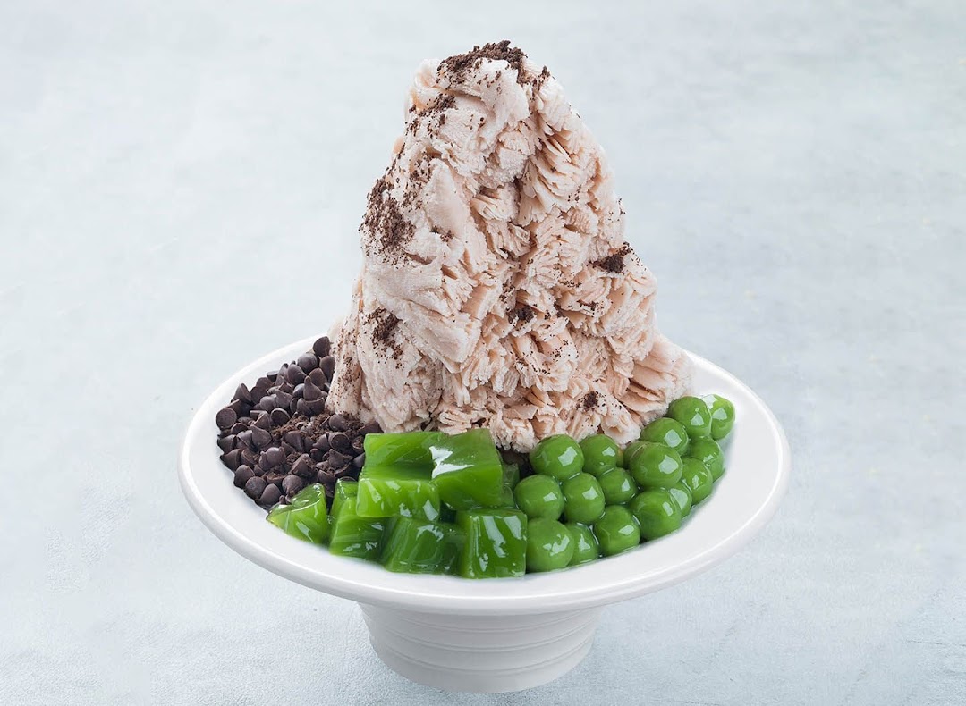 A large dessert bowl featuring fluffy shaved ice, chocolate chips, green jelly, and green pearls.
