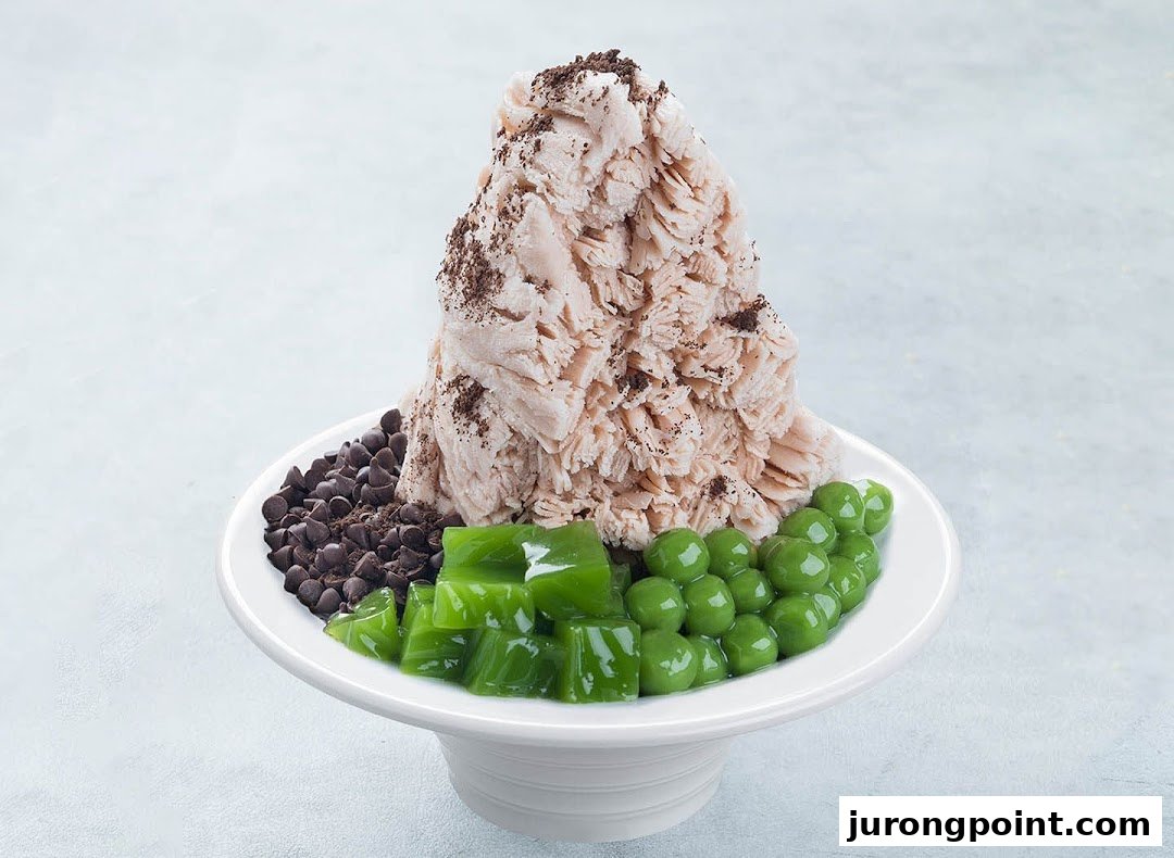 A large dessert bowl featuring fluffy shaved ice, chocolate chips, green jelly, and green pearls.