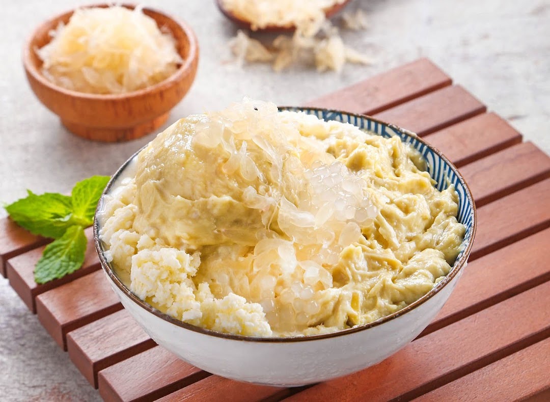 A bowl of creamy durian dessert topped with fresh pomelo, served on a wooden tray.