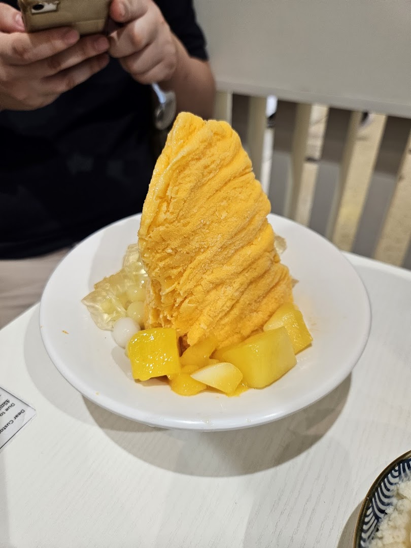 A vibrant mango shaved ice dessert with fresh mango chunks and toppings on a white table.