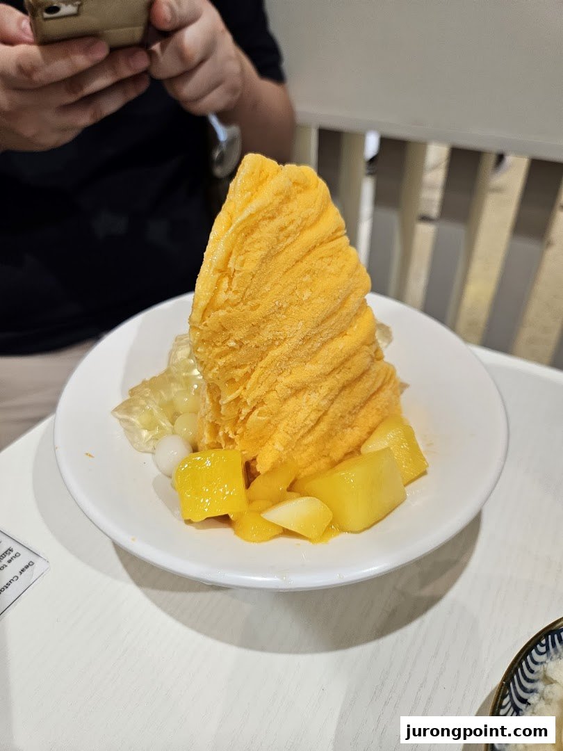 A vibrant mango shaved ice dessert with fresh mango chunks and toppings on a white table.