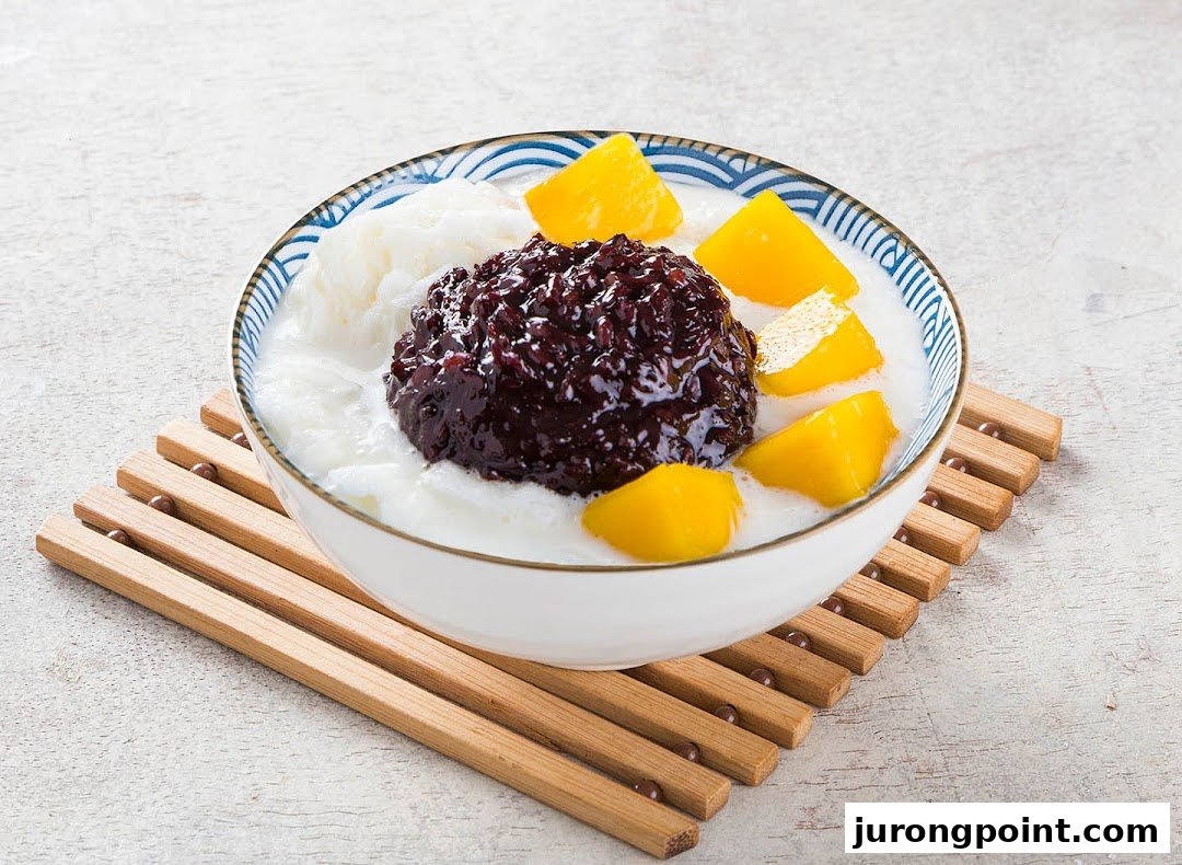 A vibrant bowl of dessert featuring black sticky rice, mango, and shaved ice on a wooden mat.