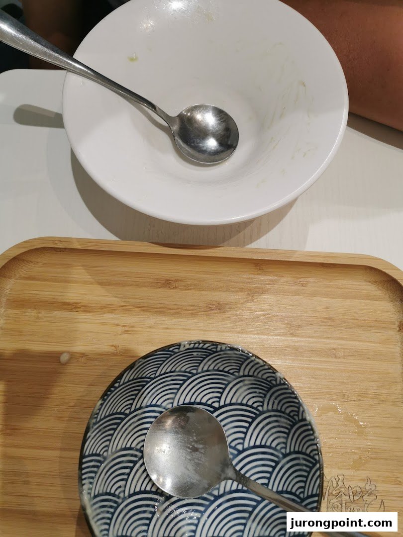 An empty dessert bowl and a small patterned plate with spoons on a wooden tray.