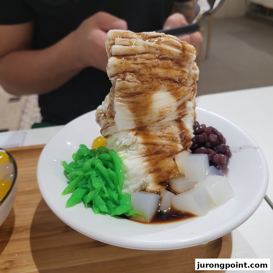 A close-up of a refreshing shaved ice dessert with red beans, green cendol, and nata de coco.