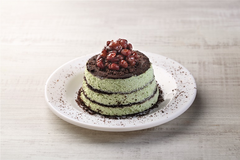 A delightful layered green dessert with chocolate crumbs and red bean topping on a white plate.