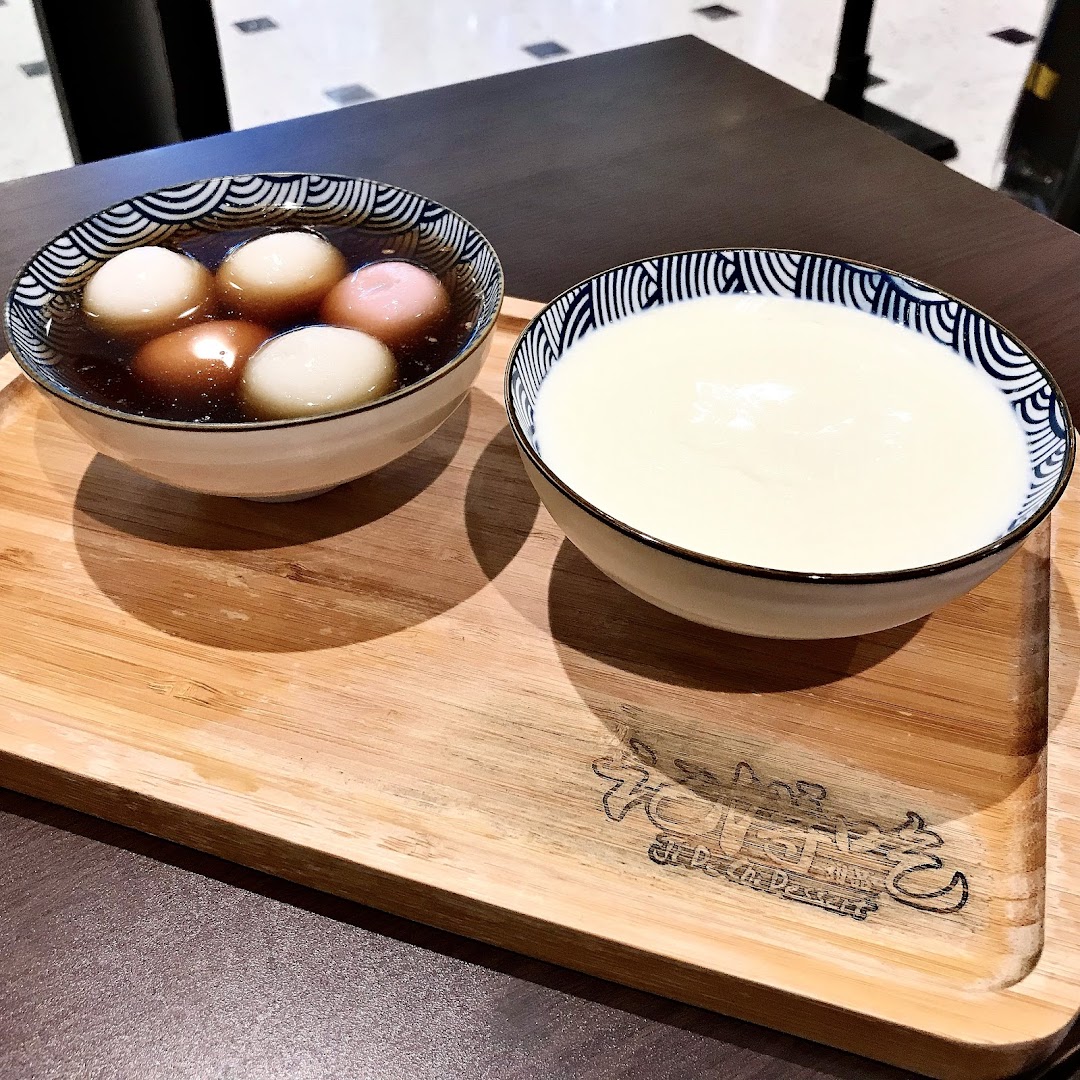 Two bowls of delicious desserts, one with tangyuan and the other with a creamy white dessert, on a wooden tray.