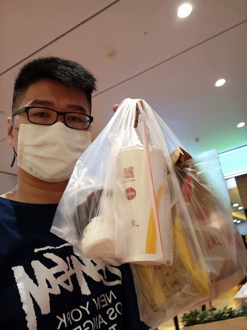 A person wearing a mask holds a plastic bag with takeaway food and drinks inside a mall.