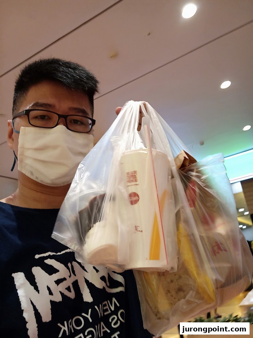 A person wearing a mask holds a plastic bag with takeaway food and drinks inside a mall.