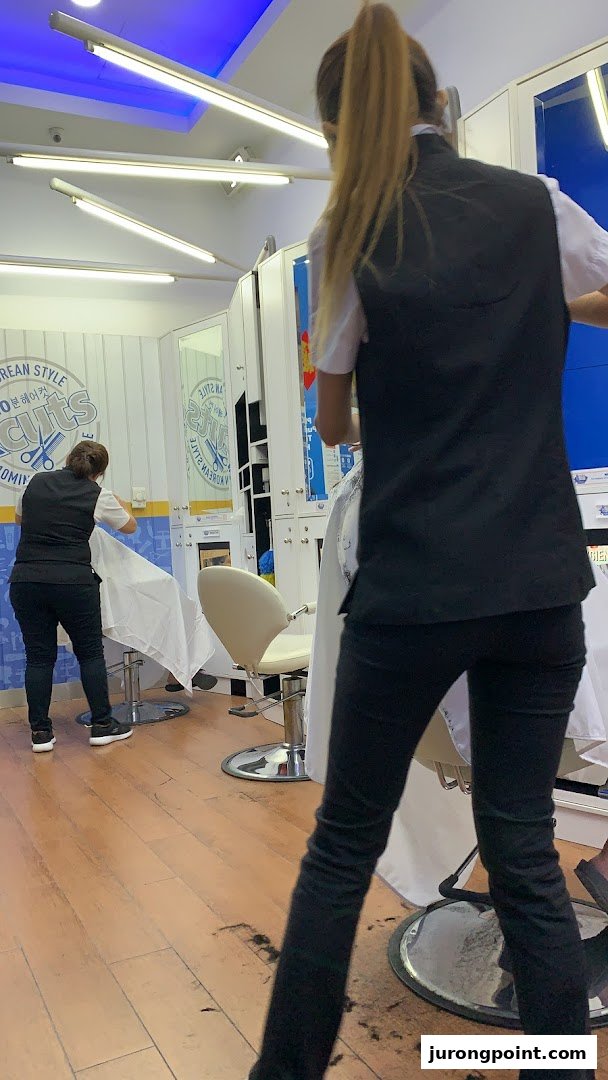 Two stylists working inside a kcuts hair salon, with chairs and mirrors visible.