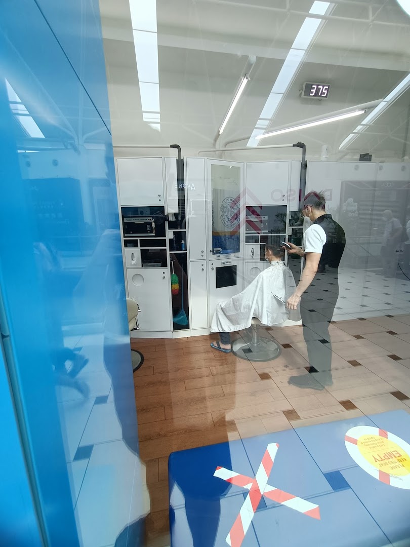 A barber cuts a customer's hair inside kcuts, viewed through a reflective glass window.