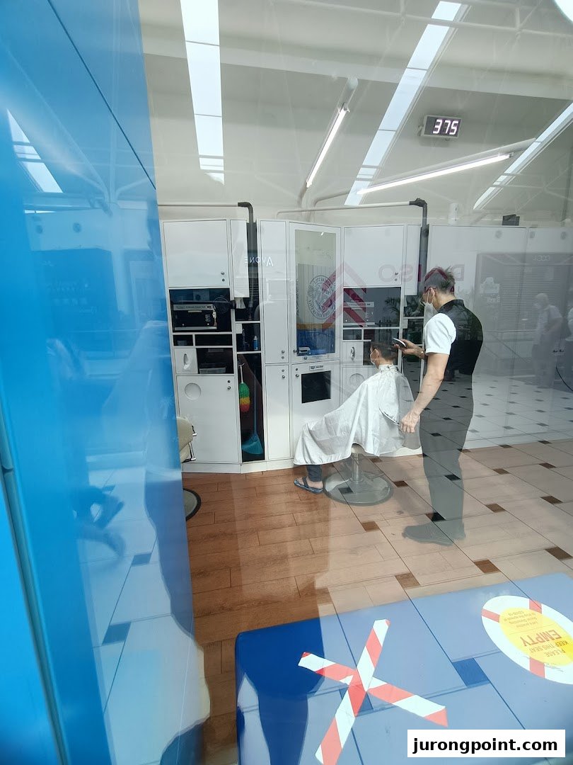 A barber cuts a customer's hair inside kcuts, viewed through a reflective glass window.