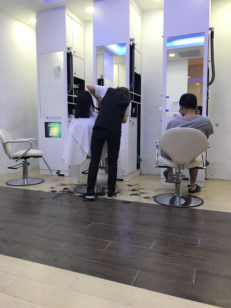A stylist provides a haircut to a customer inside kcuts, with another customer waiting.