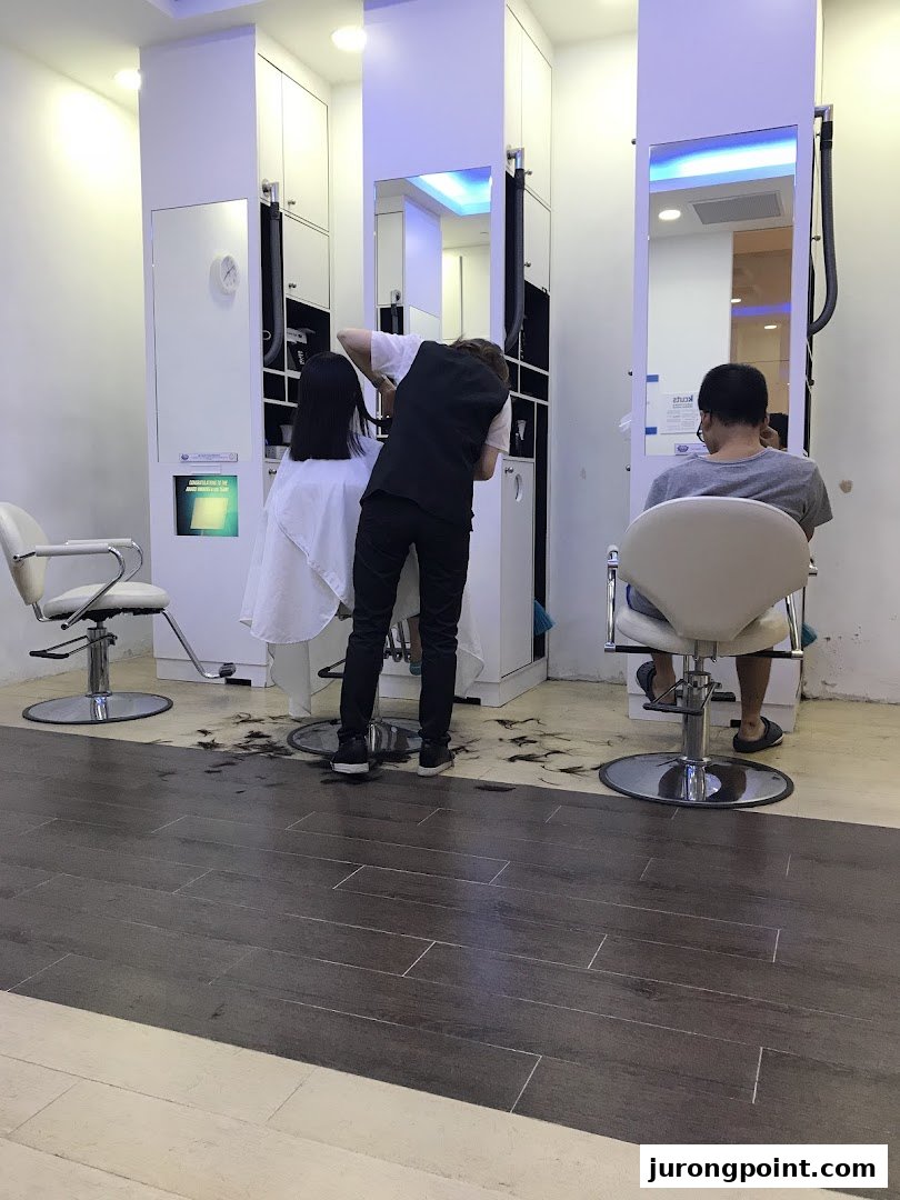 A stylist provides a haircut to a customer inside kcuts, with another customer waiting.