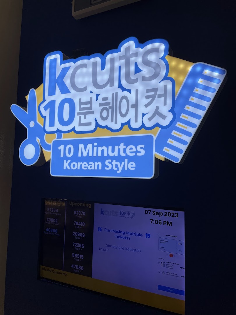 A brightly lit kcuts sign with a digital queue management system displaying wait times and service options.