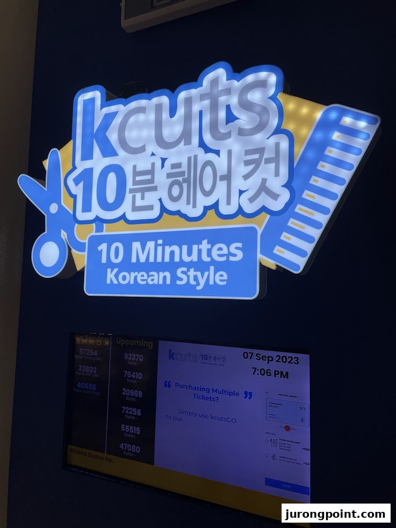 A brightly lit kcuts sign with a digital queue management system displaying wait times and service options.