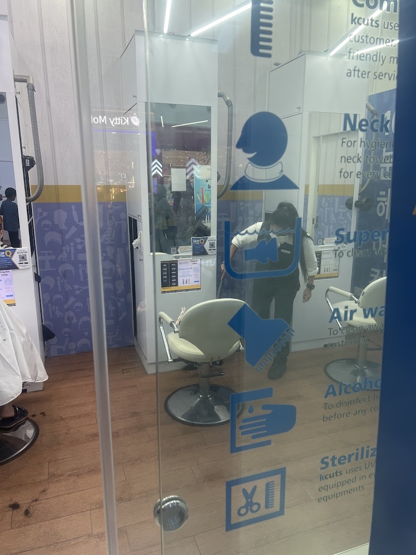 Interior view of a kcuts hair salon through a glass door, showing a staff member and barber chairs.