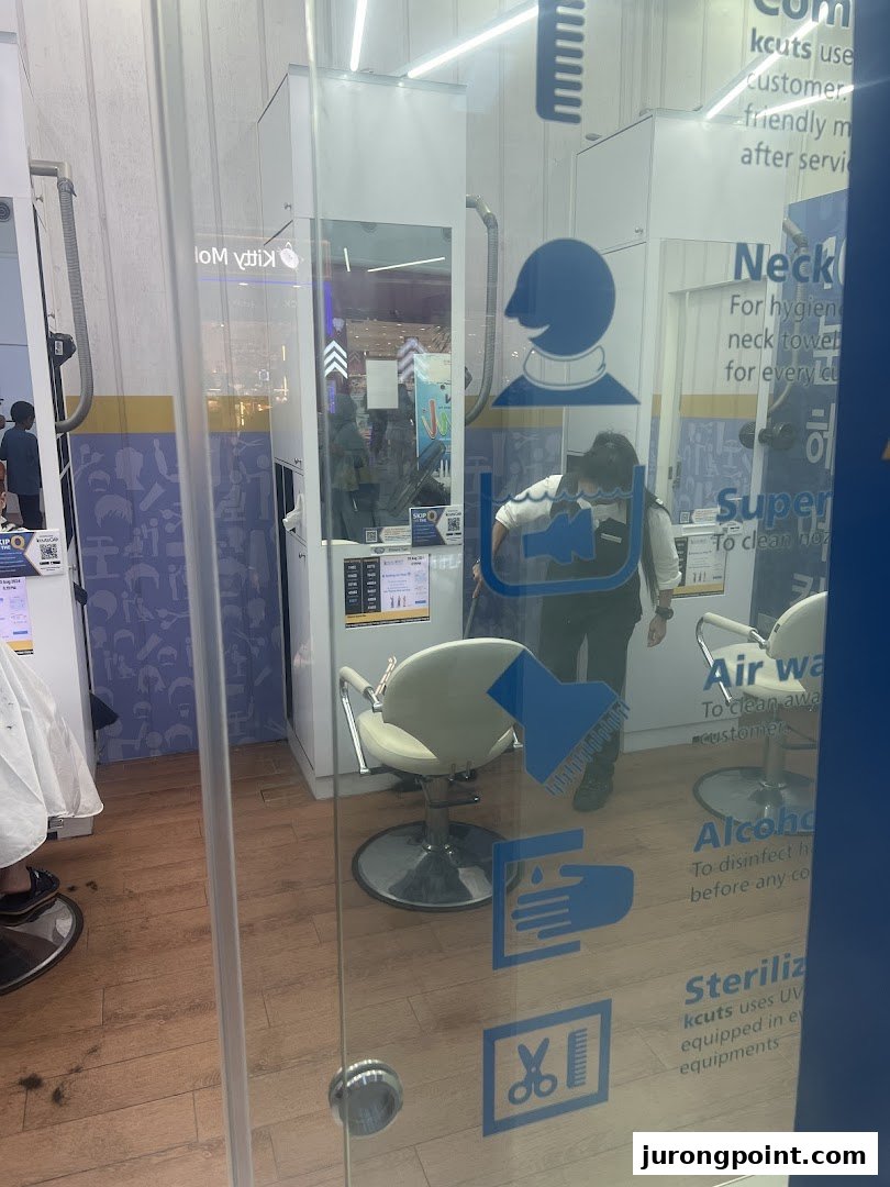 Interior view of a kcuts hair salon through a glass door, showing a staff member and barber chairs.