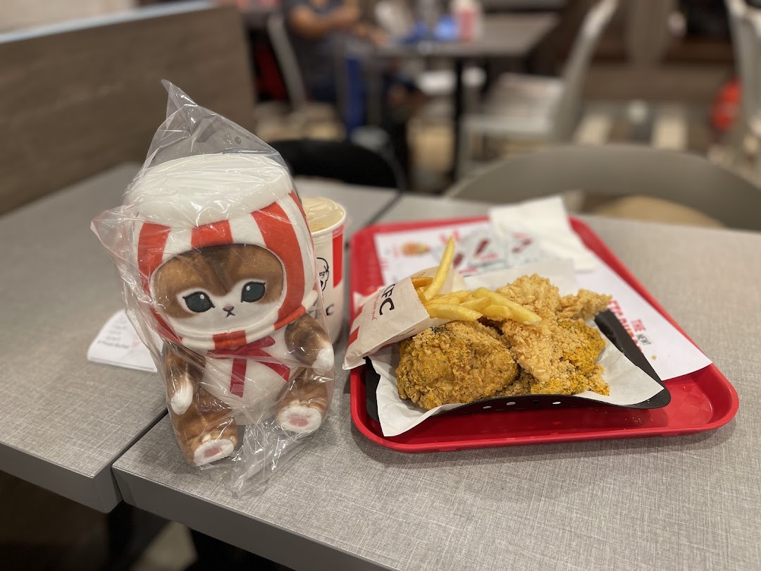 A KFC meal with fried chicken, fries, a drink, and a cute plush toy on a table.
