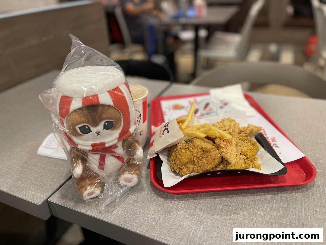 A KFC meal with fried chicken, fries, a drink, and a cute plush toy on a table.