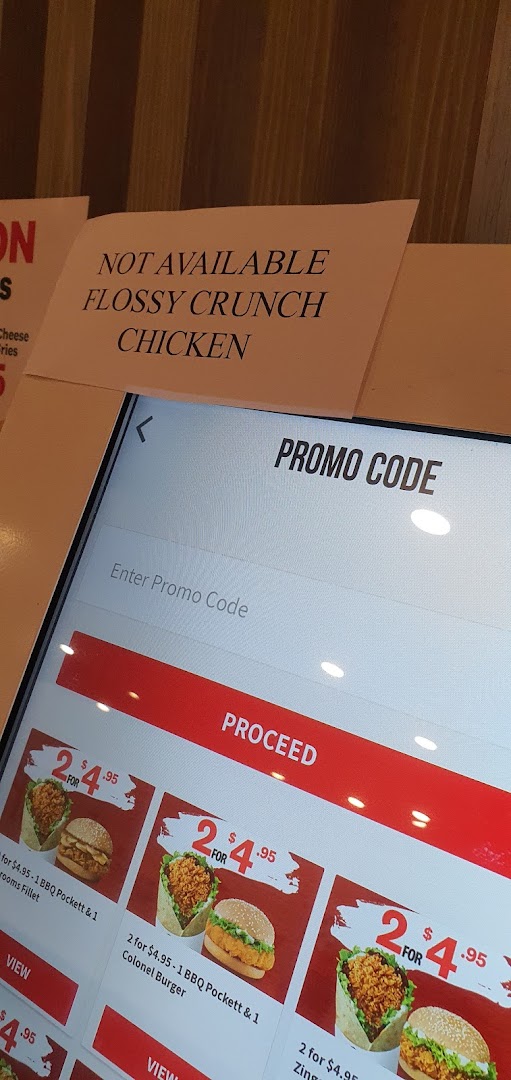 A KFC self-service kiosk displaying menu items, promotional offers, and a promo code entry screen.