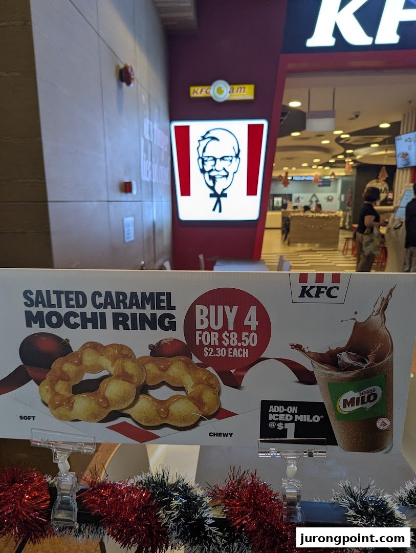 A promotional display for KFC's Salted Caramel Mochi Ring and Iced Milo at the shop entrance.