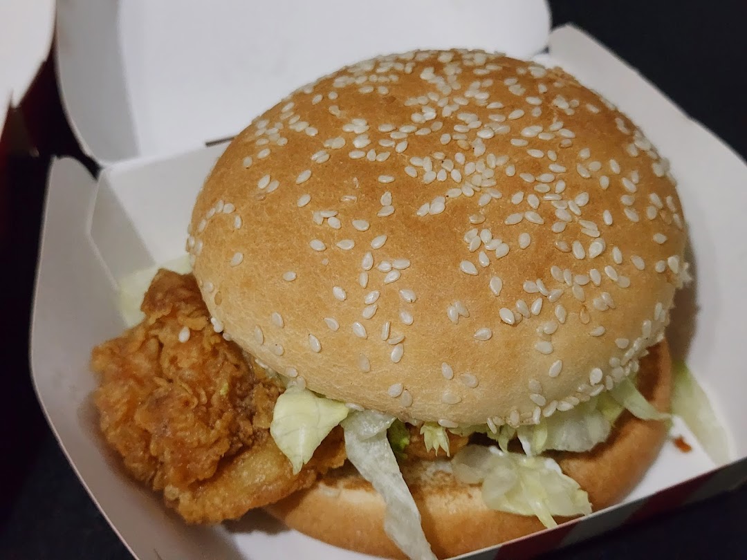 A close-up of a delicious KFC chicken burger with lettuce and a sesame seed bun in its takeaway box.