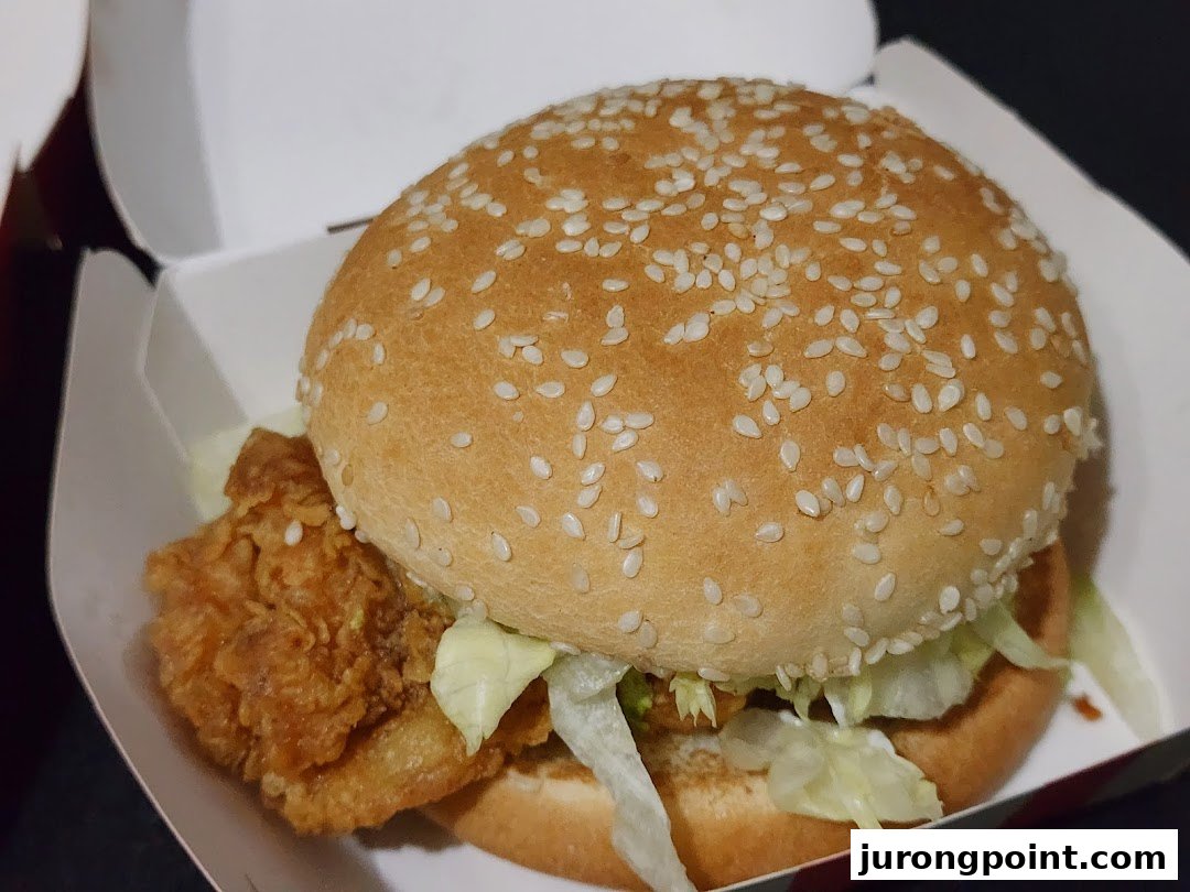 A close-up of a delicious KFC chicken burger with lettuce and a sesame seed bun in its takeaway box.