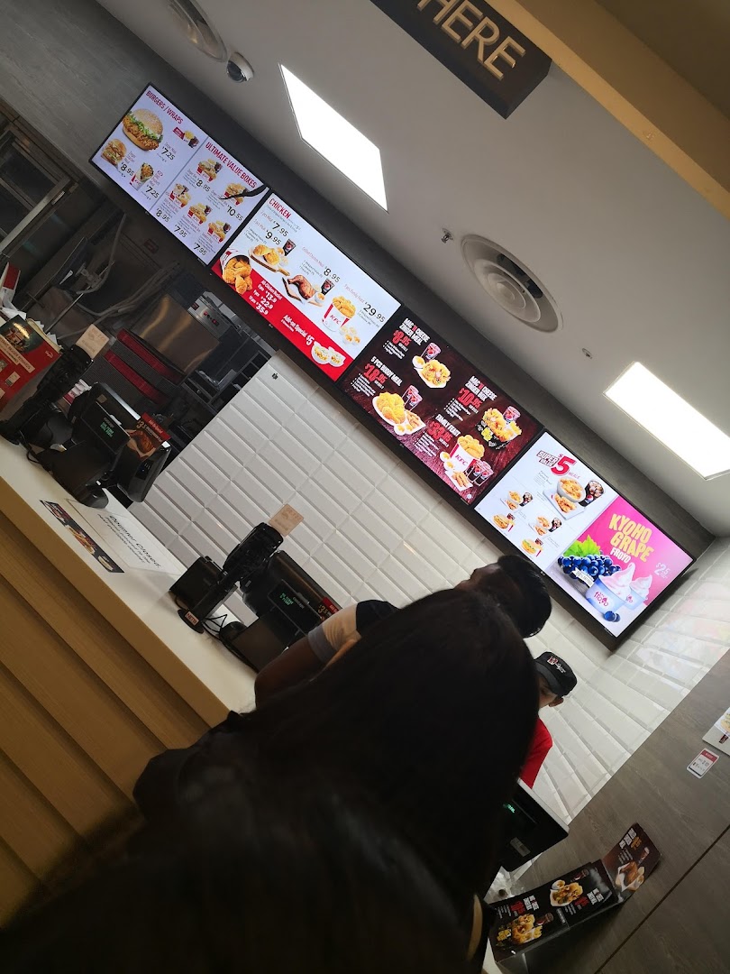 Digital menu boards display KFC's offerings above a busy counter with customers waiting to order.