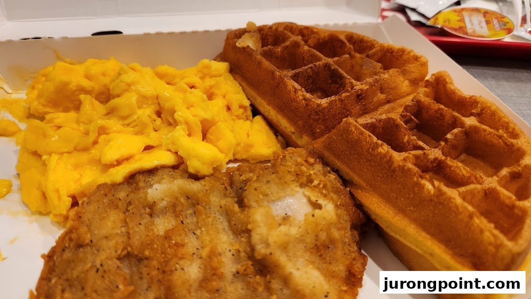 A close-up of KFC's fried chicken, waffles, and scrambled eggs in a takeout box.