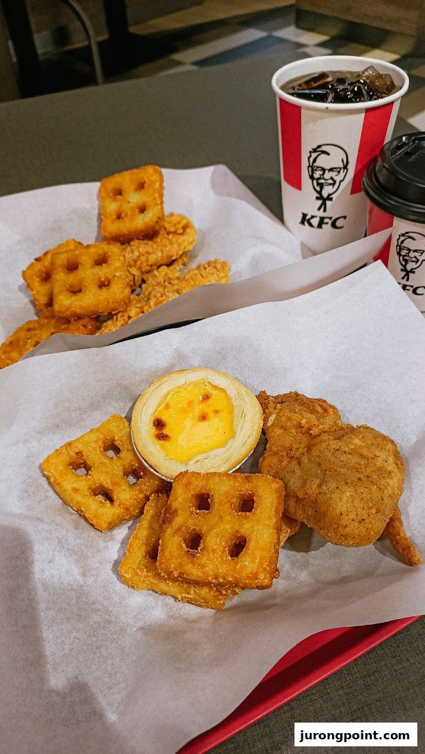 A delicious spread of KFC fried chicken, waffle fries, an egg tart, and refreshing drinks.