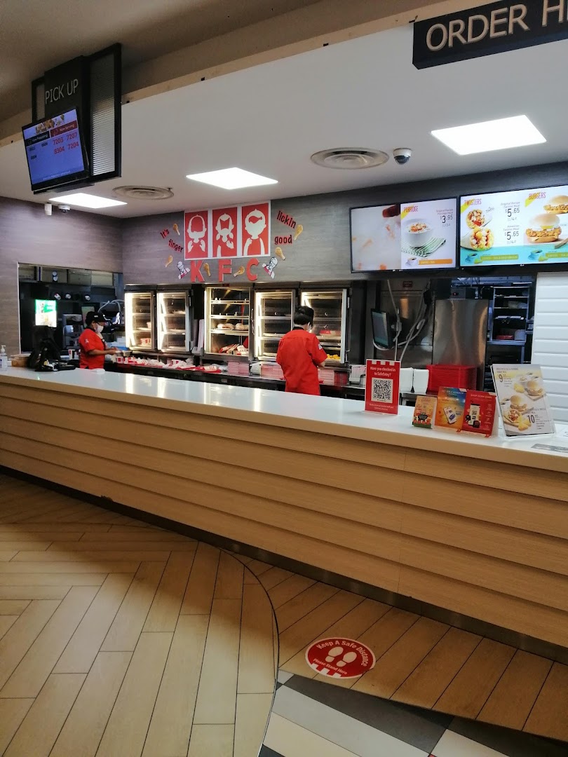 KFC's bustling counter area with staff, food displays, and digital menu screens.