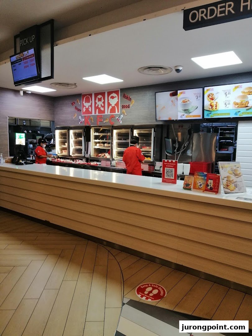 KFC's bustling counter area with staff, food displays, and digital menu screens.