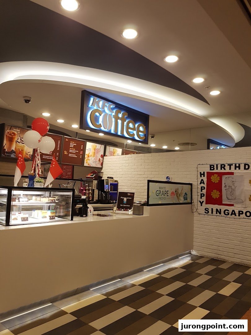 Interior view of KFC Coffee counter with a display case, menu boards, and a 'Happy Birthday Singapore' banner.