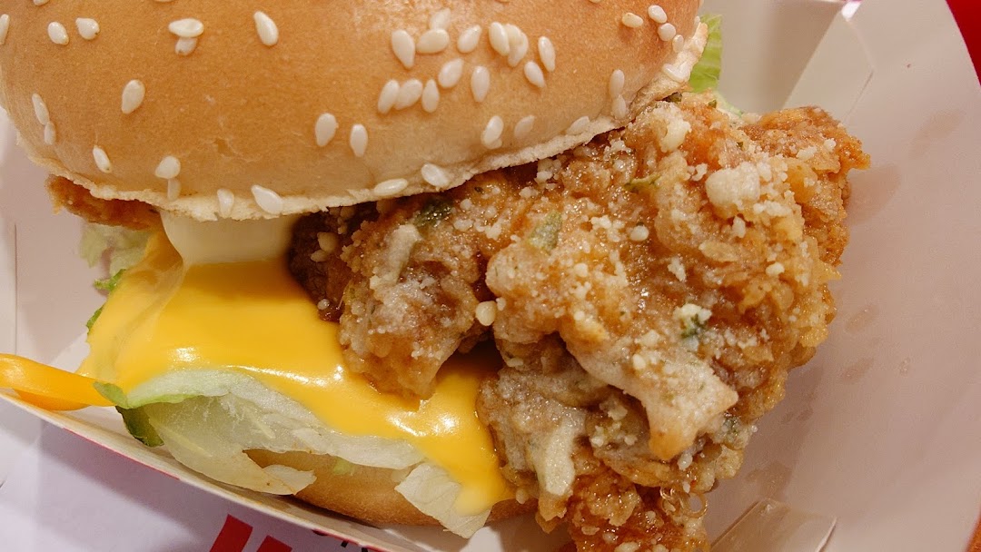 A close-up of a crispy fried chicken burger with melted cheese and lettuce in a sesame seed bun.