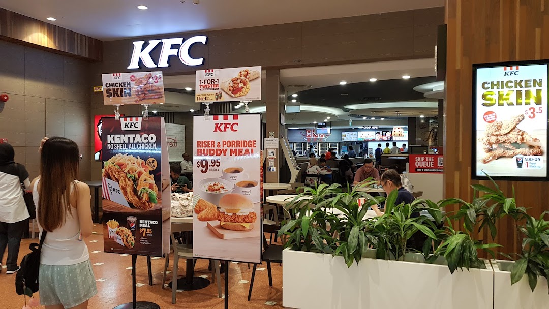 A bustling KFC outlet entrance in a mall, featuring promotional displays and customers dining inside.