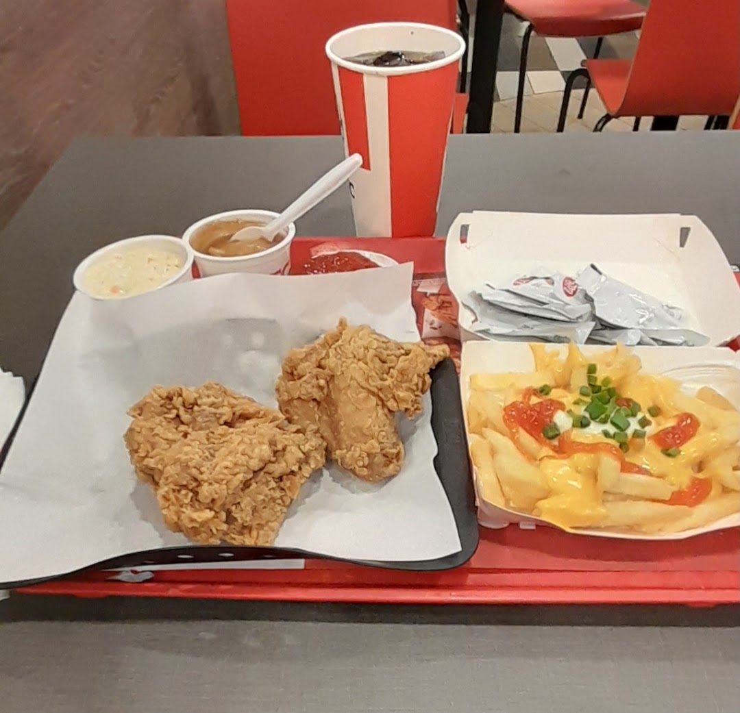 A delicious KFC meal featuring fried chicken, cheesy fries, coleslaw, gravy, and a drink on a red tray.