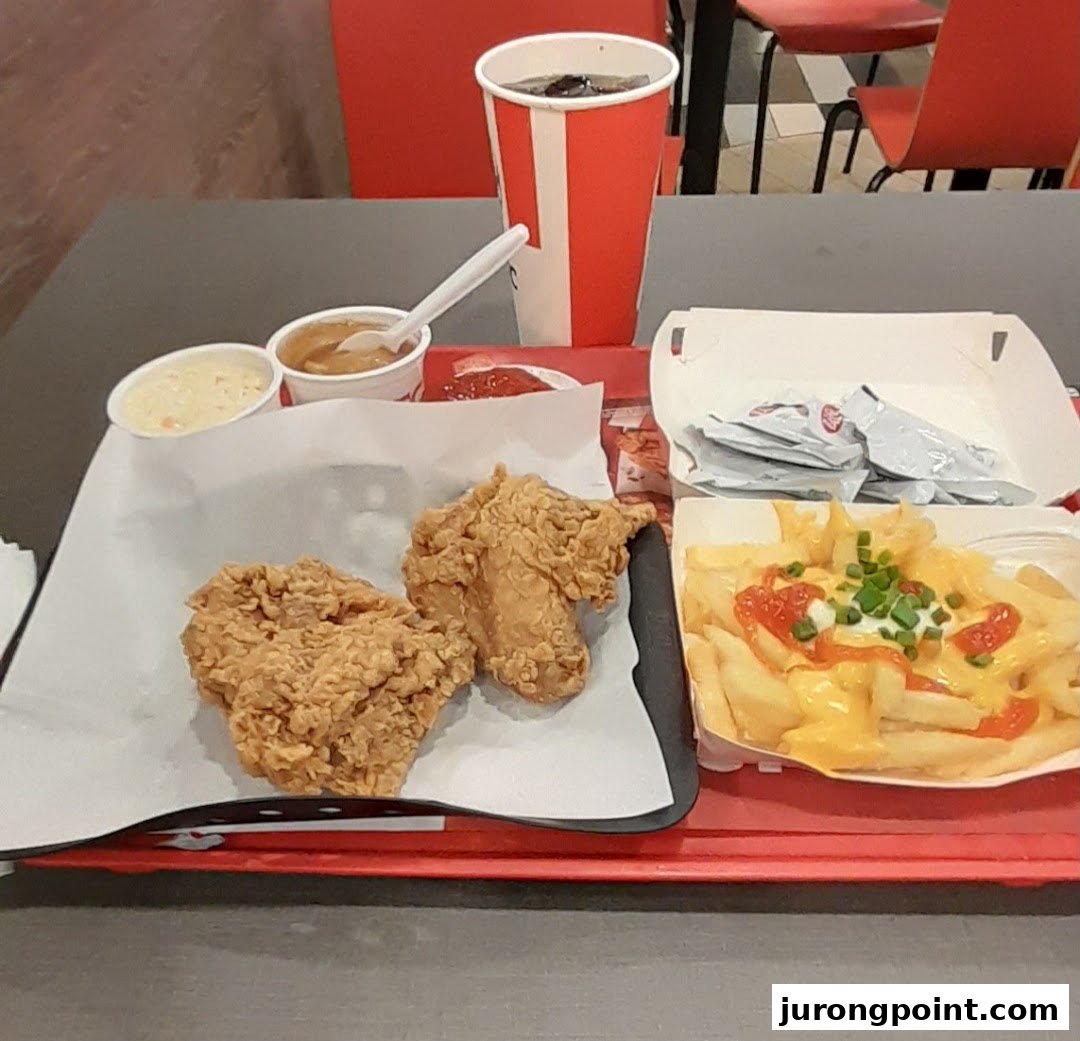 A delicious KFC meal featuring fried chicken, cheesy fries, coleslaw, gravy, and a drink on a red tray.
