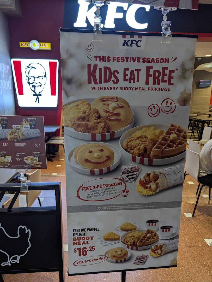 A KFC promotional standee advertises 'Kids Eat Free' with Buddy Meal purchases and breakfast items.