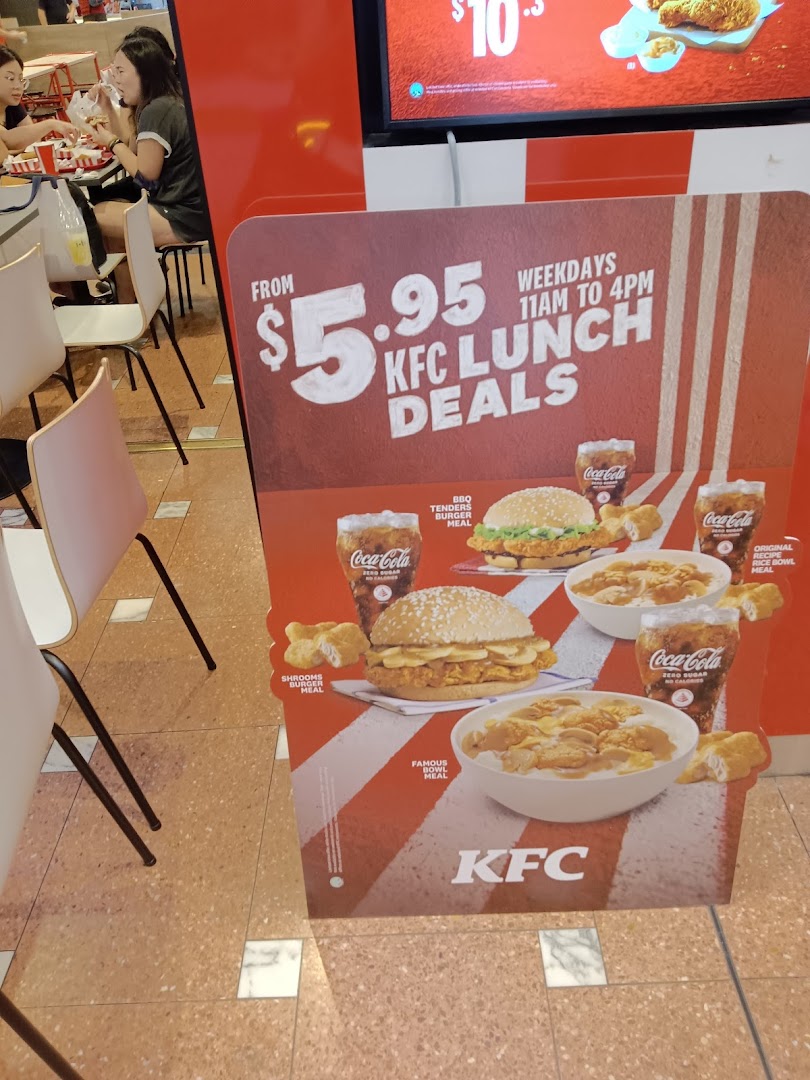 A promotional sign for KFC Lunch Deals with customers dining in the background.